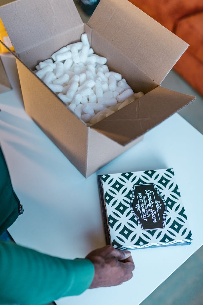 Open cardboard box with packing peanuts and hand placing patterned item.
